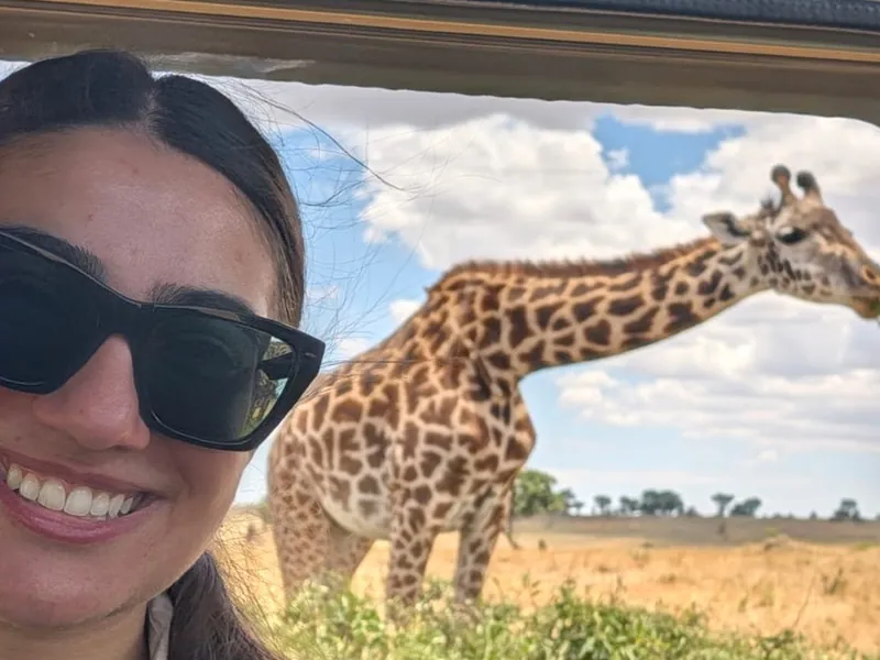 A guest smiling in the safari vehicle, with a giraffe outside the window