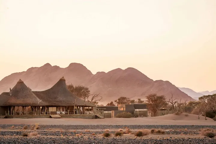 Thatched suites against a mountain backdrop at Little Kulala in warm evening light