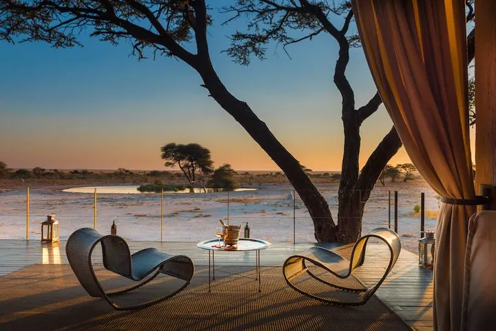 Chairs on a timber deck with an acacia tree against a sunset sky at Onguma The Fort