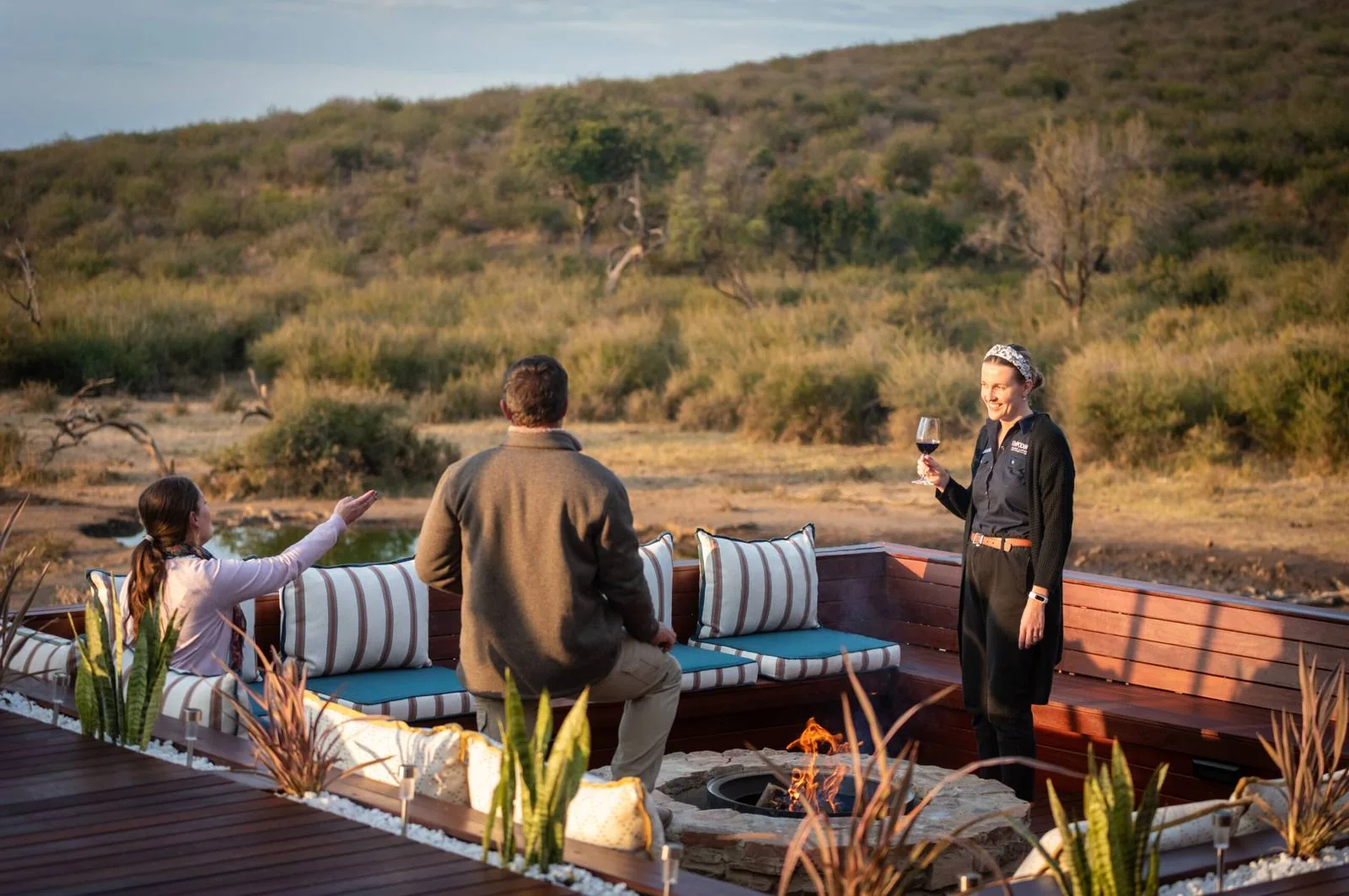 Guests around a fire pit above a waterhole at Impodimo Game Lodge, Madikwe