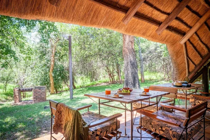 A thatched veranda with a dining table looking onto the garden at Lokuthula Lodges