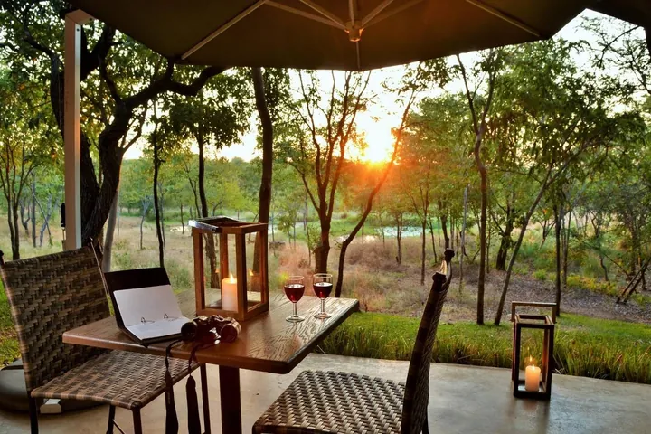 A deck at sunset with wine glasses and lanterns at Victoria Falls Safari Suites