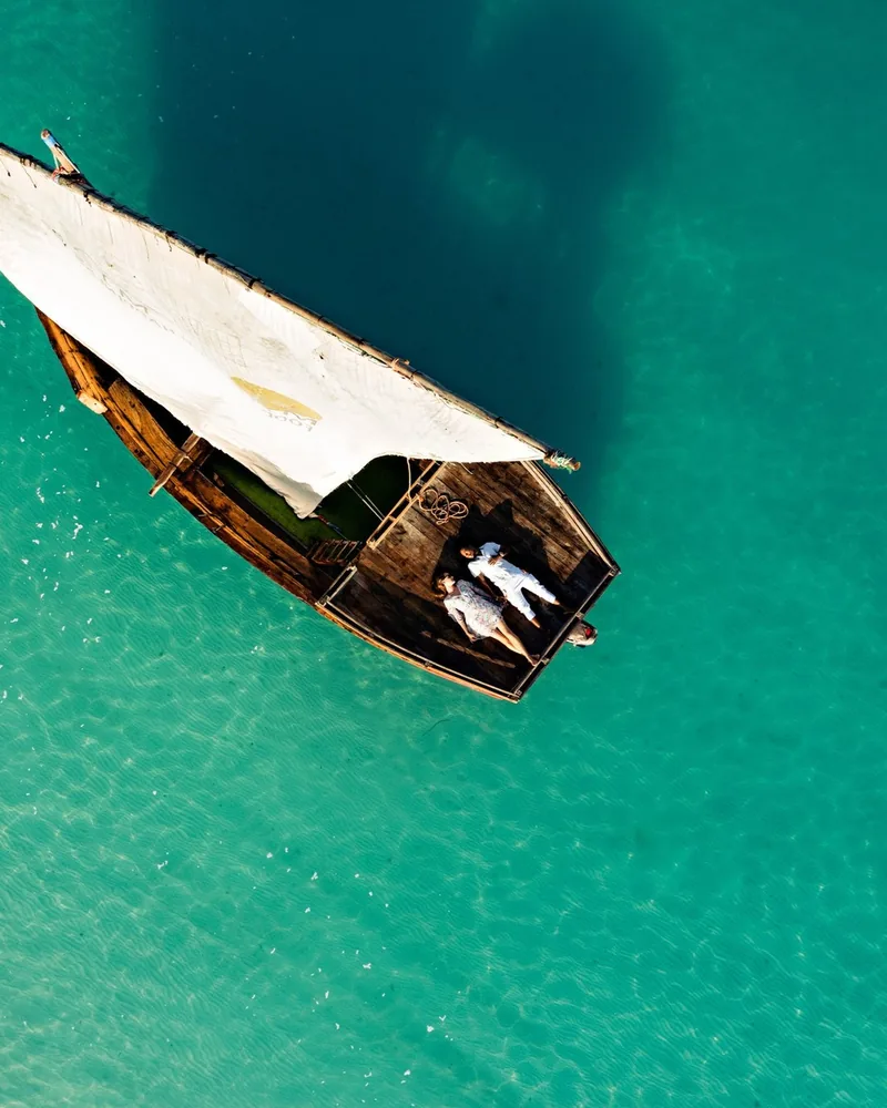 A wooden dhow on clear turquoise water, seen from above